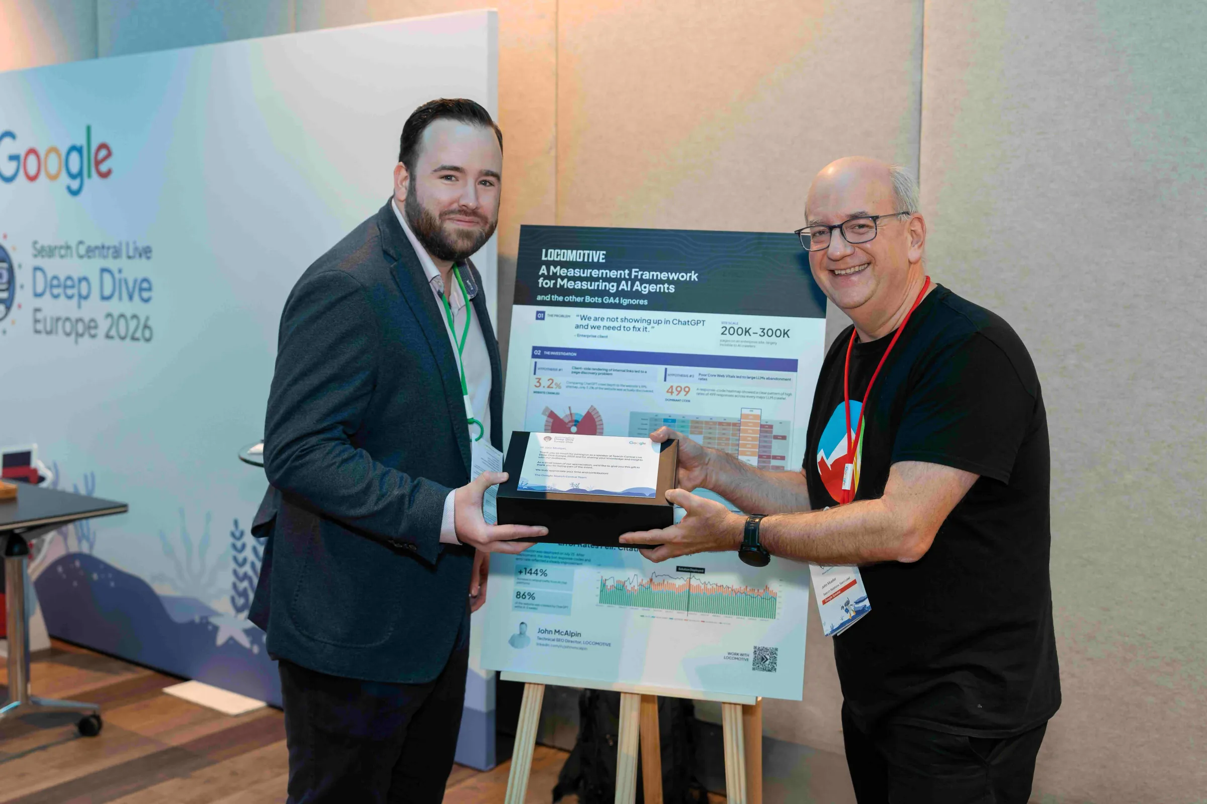 John McAlpin receiving a speaker gift from Google's John Mueller in front of his poster